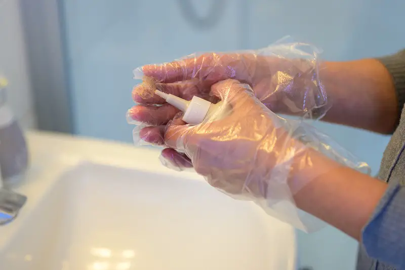 woman mixing a bottle of hair dye in a bathroom as she prepares to apply coloring to her hair with gloved hands in close up