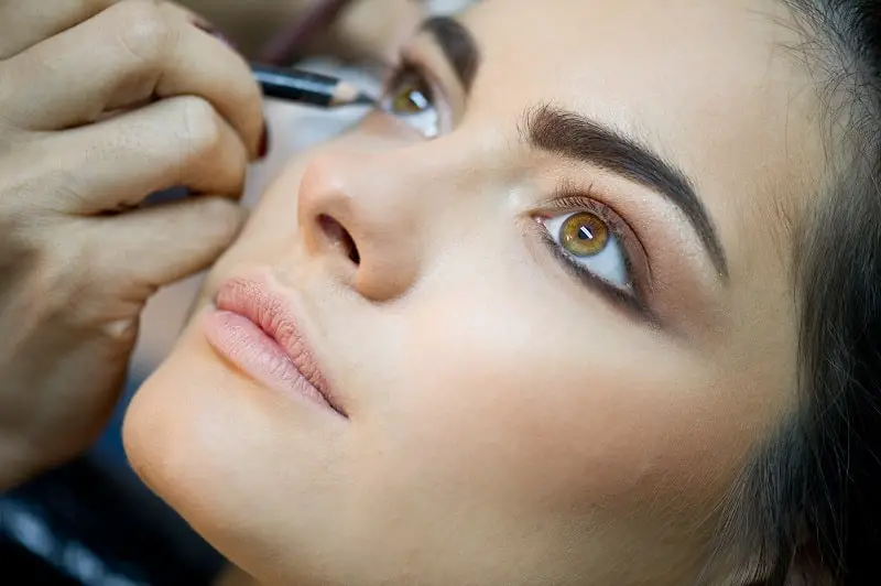 close-up of a young woman getting eyeliner applied to her eyes