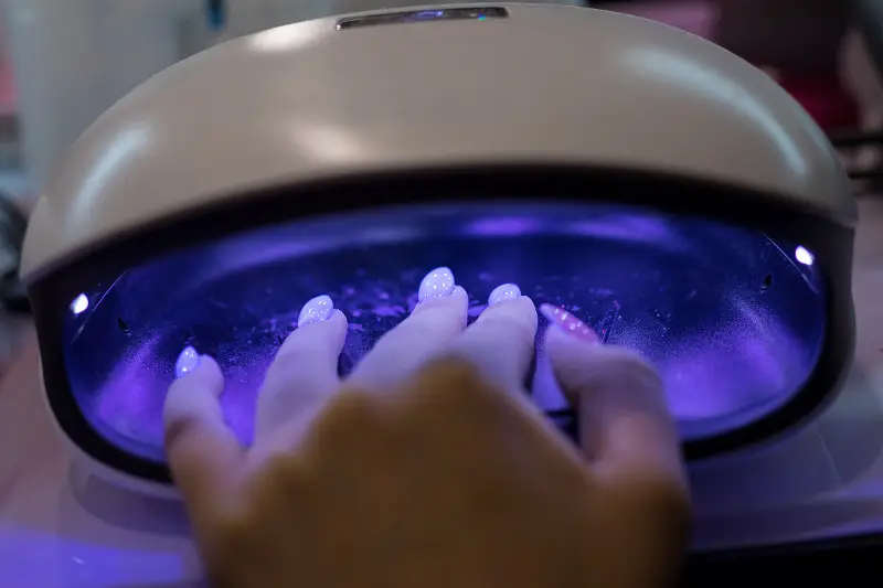 young woman's hand in polygel nail drying machine in nail salon