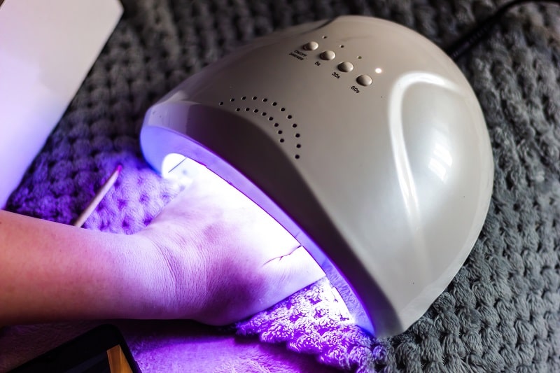 woman curing her polygel nails by using an LED nail lamp at home