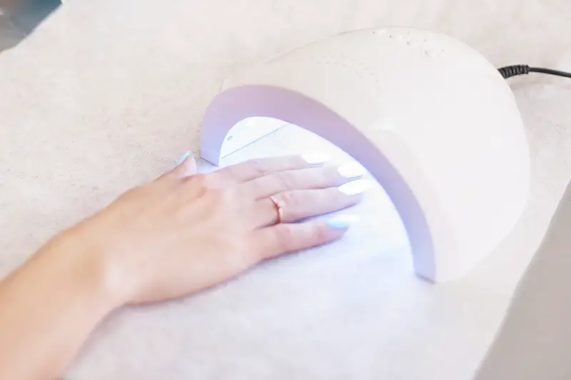 close-up of a woman using a UV nail light to prevent her polygel nails from popping off