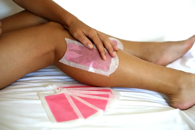woman with a sunbed tan waxing her legs with wax stripe at home
