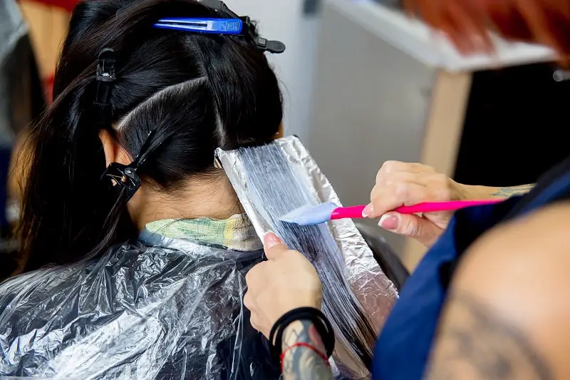 close-up of a hairdresser coloring the luscious locks of a stunning young woman, applying hair dye to individual strands with a brush on aluminium foil